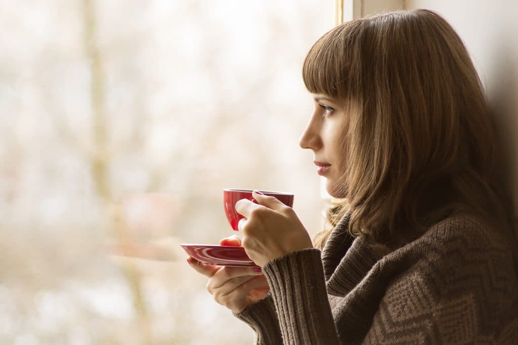 Vacker flicka som dricker kaffe eller te nära fönstret