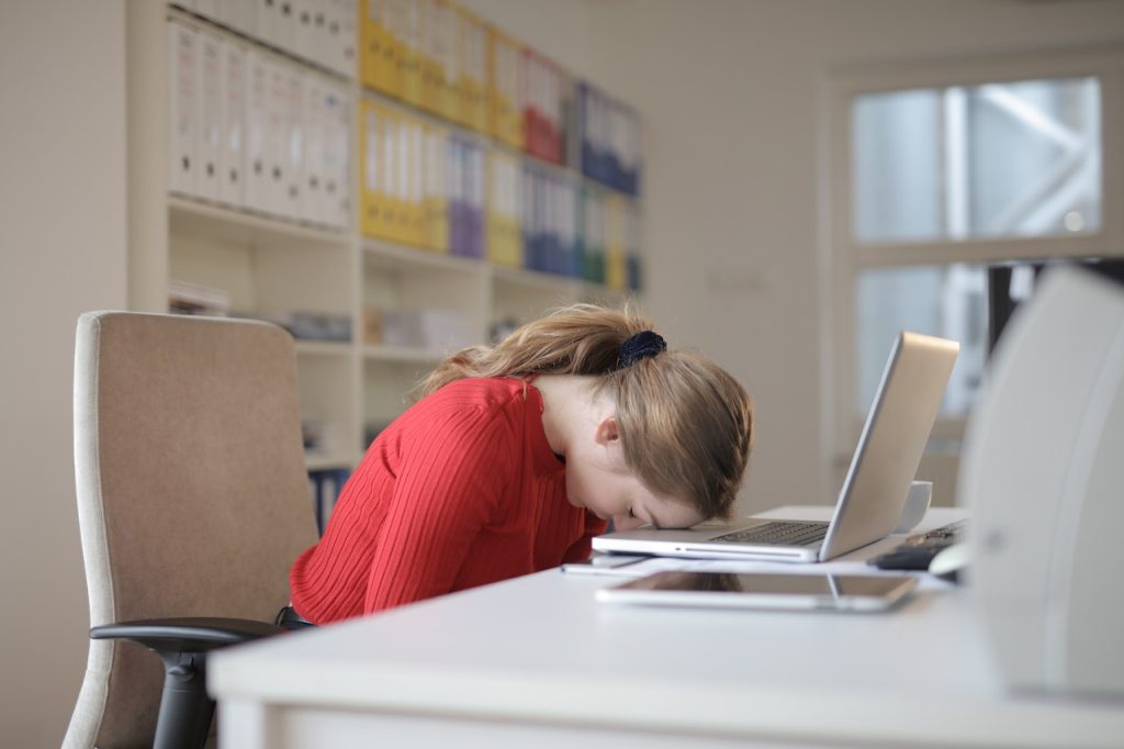 trött kvinna lutar huvudet mot sin dator för att visa sin känslomässiga eller vintertrötthet