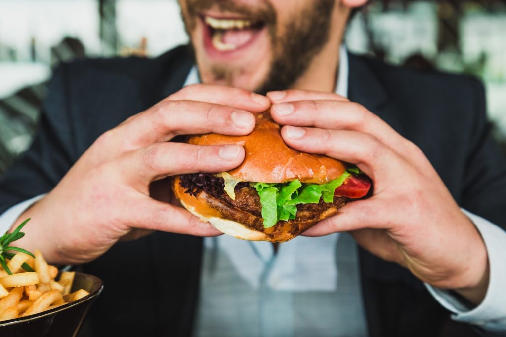 person som håller hamburgerbulle med grönsaker och kött